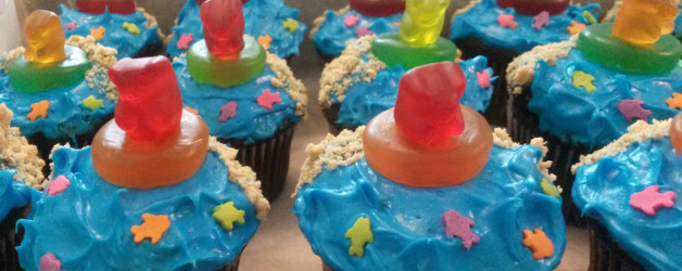 cupcakes decorated with blue 'sea' frosting, has sand and gummy bears in lifesavers
